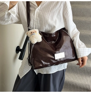 Detailed view of glossy dark brown tote bag with metallic logo and plush bear charm