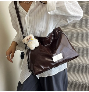 Detail of dark brown glossy tote bag with metal zipper and white bear charm on model