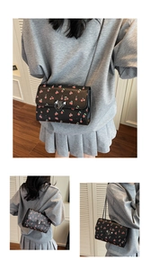 Détail du motif cerise sur le sac à bandoulière noir avec chaîne en métal argenté