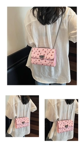 Détail d'un sac bandoulière rose avec motifs cerises et bandoulière chaîne sur un mannequin