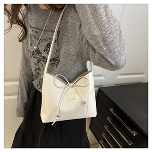 Detail der weißen glänzenden Ledertasche mit großer Schleife und Metallkugel-Anhänger
