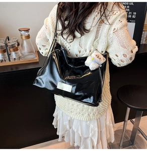 Detail of black glossy tote bag featuring silver hardware and a white plush bear charm