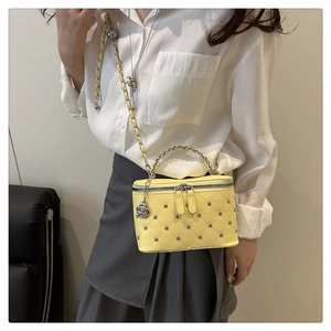 Detail of yellow quilted crossbody bag with silver studs and rose charm accessory