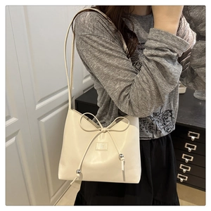 Detail der cremeweißen PU-Leder Beuteltasche mit Schleife und Metallperlen am Model