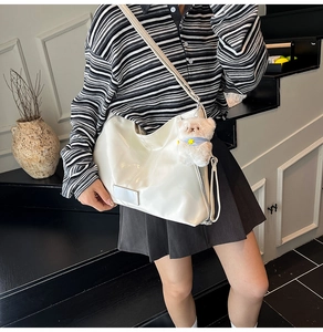 Detailed view of white patent leather tote bag with metallic logo and plush bear charm