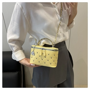 Close-up of a yellow quilted bucket bag with silver studs and a chain handle on a model