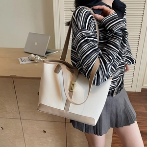 Large beige tote bag with brown trim and gold buckle worn on shoulder in office setting