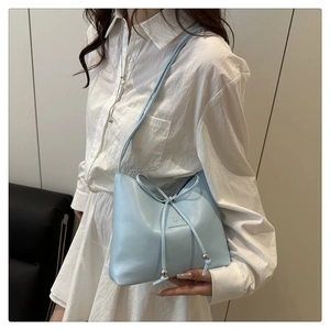 Modell mit hellblauer Halbmond-Schultertasche, Schleifen-Etikett und Metallkugel-Verzierungen