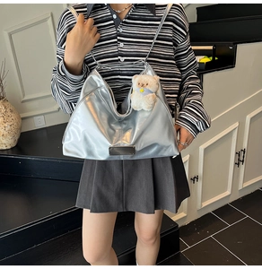 Silver metallic hobo bag with plush bear charm worn by model on a modern staircase