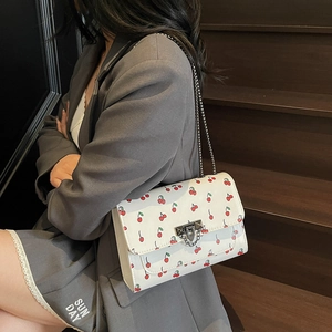 Sac à bandoulière en cuir blanc avec imprimé cerises et chaîne argentée sur escalier