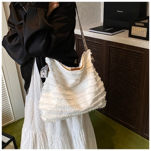 Makro-Detail der weißen Segeltuch-Strohtasche mit Fransenschichten und kariertem Trageriemen