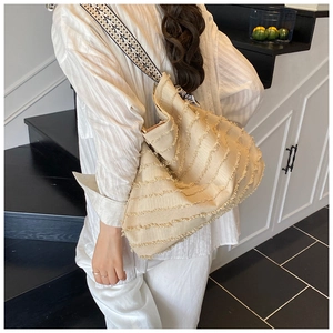 Detail der beigen Strohtasche mit Fransenstruktur und geometrischem Tragegurt