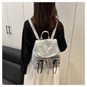 Détail d'un sac à dos argenté métallisé avec des nœuds en soie noire et broderie Nika