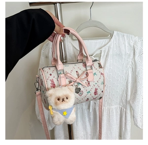 Detail of cute cream Boston bag with pink rabbit prints and a white plush bear charm