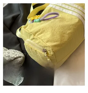 Detailed close-up of yellow nylon gym bag featuring white stripes and purple zipper puller