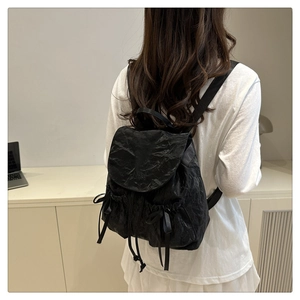 Close-up of black nylon backpack featuring side bow details and pleated fabric texture