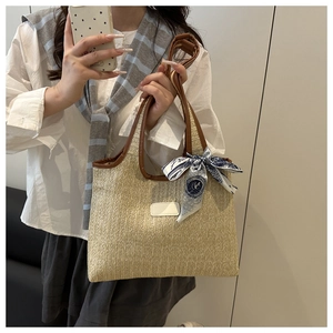 Detail of beige straw tote bag featuring brown leather handles and a blue printed silk scarf