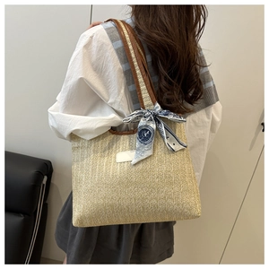Close-up of woven straw tote bag with brown leather straps and patterned blue silk scarf