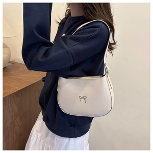 Detail of a creamy white hobo bag showing the silver bow hardware and leather texture