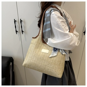 Detail of woven straw tote bag with brown leather trim and blue patterned silk scarf