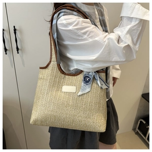 Detail of woven straw tote bag with brown leather trim and blue floral silk scarf handle