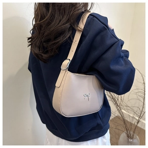 Detail of a beige crescent underarm bag with a silver bow buckle on model shoulder