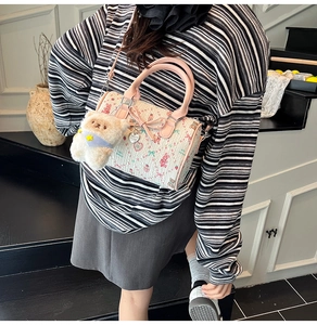 Detail of white Boston bag with pink rabbit prints and a plush bear pendant