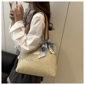 Detail of straw tote bag featuring brown leather handles and blue paisley silk scarf decor
