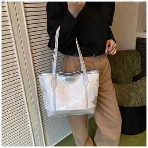 Détail du sac cabas brodé avec anses argentées et étiquette de mode sur le devant