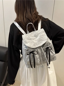 Silver pleated backpack with black satin bows and metallic finish on a female model