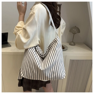 Detailed view of the large striped canvas tote bag worn over a model's shoulder