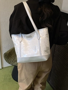 Sac fourre-tout en toile brodée blanche avec étiquette argentée porté à l'épaule