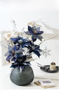 Deep blue and cream poinsettia flowers with silver glitter in dark green glass vase
