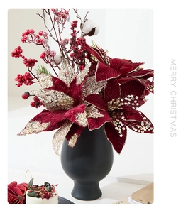 Detail of red poinsettia with gold sequins and berries in a black matte ceramic vase