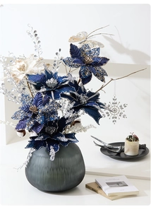 Detailed Christmas floral arrangement with blue poinsettia and grey frosted glass vase