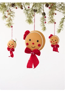 Three plush gingerbread man ornaments hanging on a pine branch with festive red berries