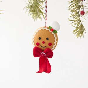 Plush Gingerbread Man Christmas tree ornament with a red velvet bow on a pine branch
