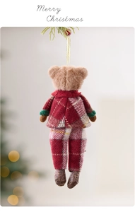 Close-up of a cute plush Christmas bear ornament hanging on a pine branch with soft bokeh