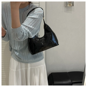 Polished black patent leather baguette bag shown against minimalist fashion attire
