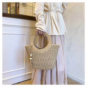 Close-up of woven straw tote with round handles, stripes and white beaded tassel detail
