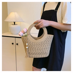Detail of woven straw bucket bag featuring round handles and white beaded tassels