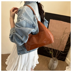 Close-up of caramel brown patent leather hobo bag worn on shoulder in a cozy setting