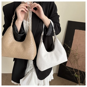 Two woven texture hobo bags in beige and white held by a model in a minimalist setting