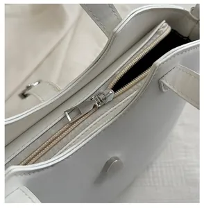 Close-up of a smooth silver zipper and stitching on a white faux leather tote bag