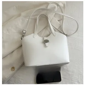 Detail view of white minimalist leather bag with round metal buckle and silk scarf accent