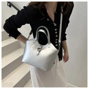 Detail of silver metallic tote bag with buckle closure worn by a model on white stairs