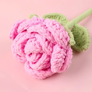 Macro shot of handmade crochet pink rose with soft chenille yarn petals and green leaves