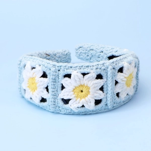 Detail of light blue hand-knitted headband with three 3D white daisy floral patterns