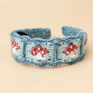 Detail of hand-knitted blue headband featuring red mushroom embroidery and soft crochet texture