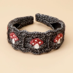 Macro detail of knit headband with red mushroom patterns on dark grey woolen texture